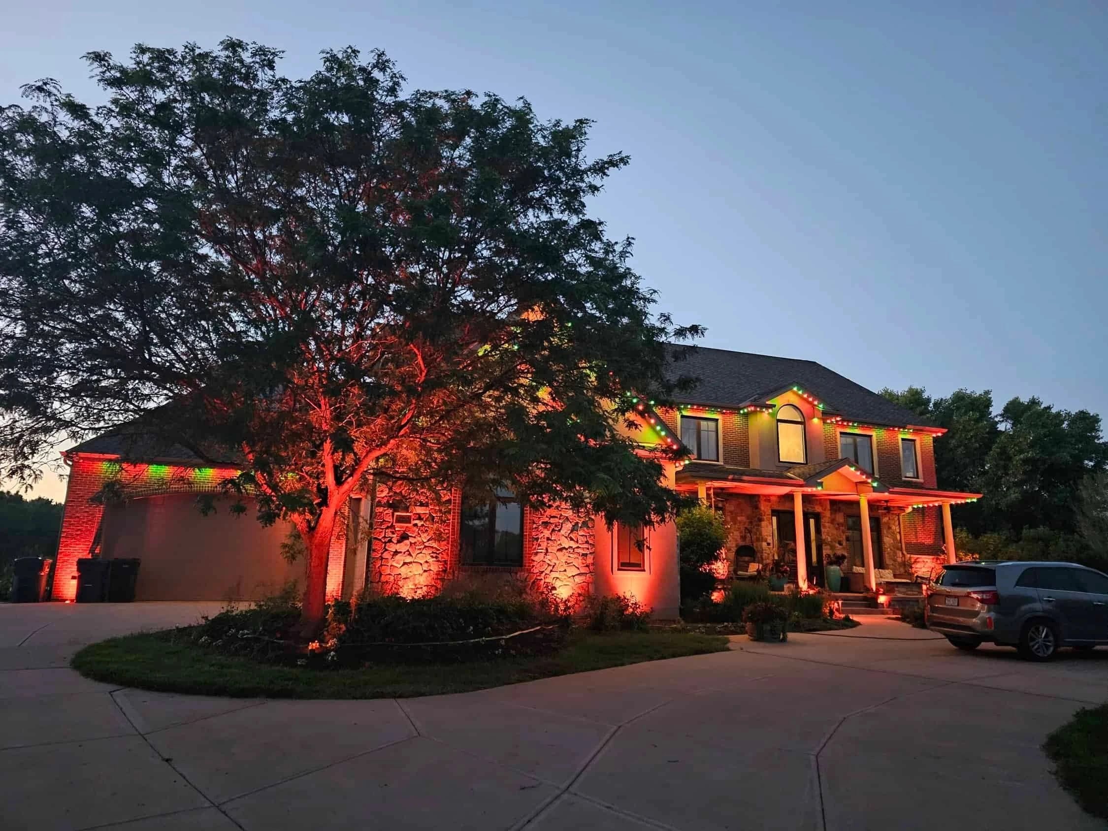 Stone home lit red and orange from the roofline on a tree-lined drive