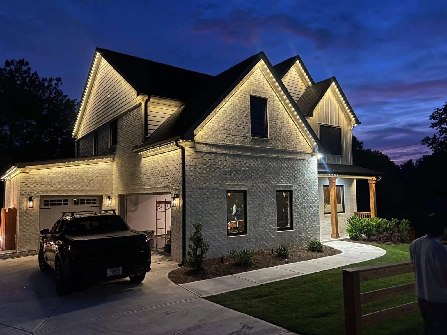 Brick two-story home with warm white permanent lighting along every gable and eave