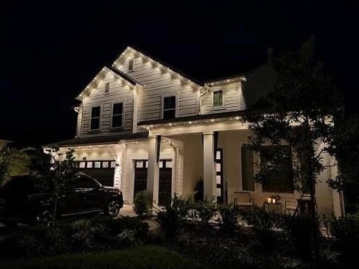 White farmhouse outlined in warm white permanent roofline lighting at night